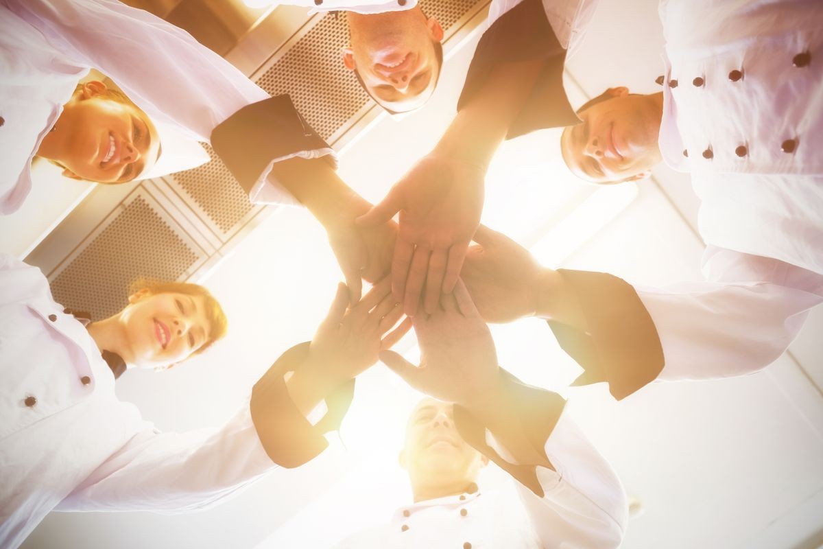 Chefs joining hands in a circle wearing uniforms in a kitchen